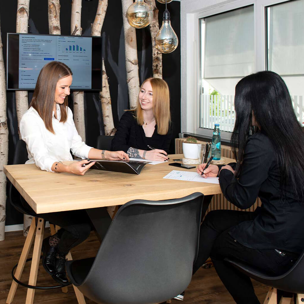 Drei Frauen sitzen an einem Tisch zur Teambesprechung.